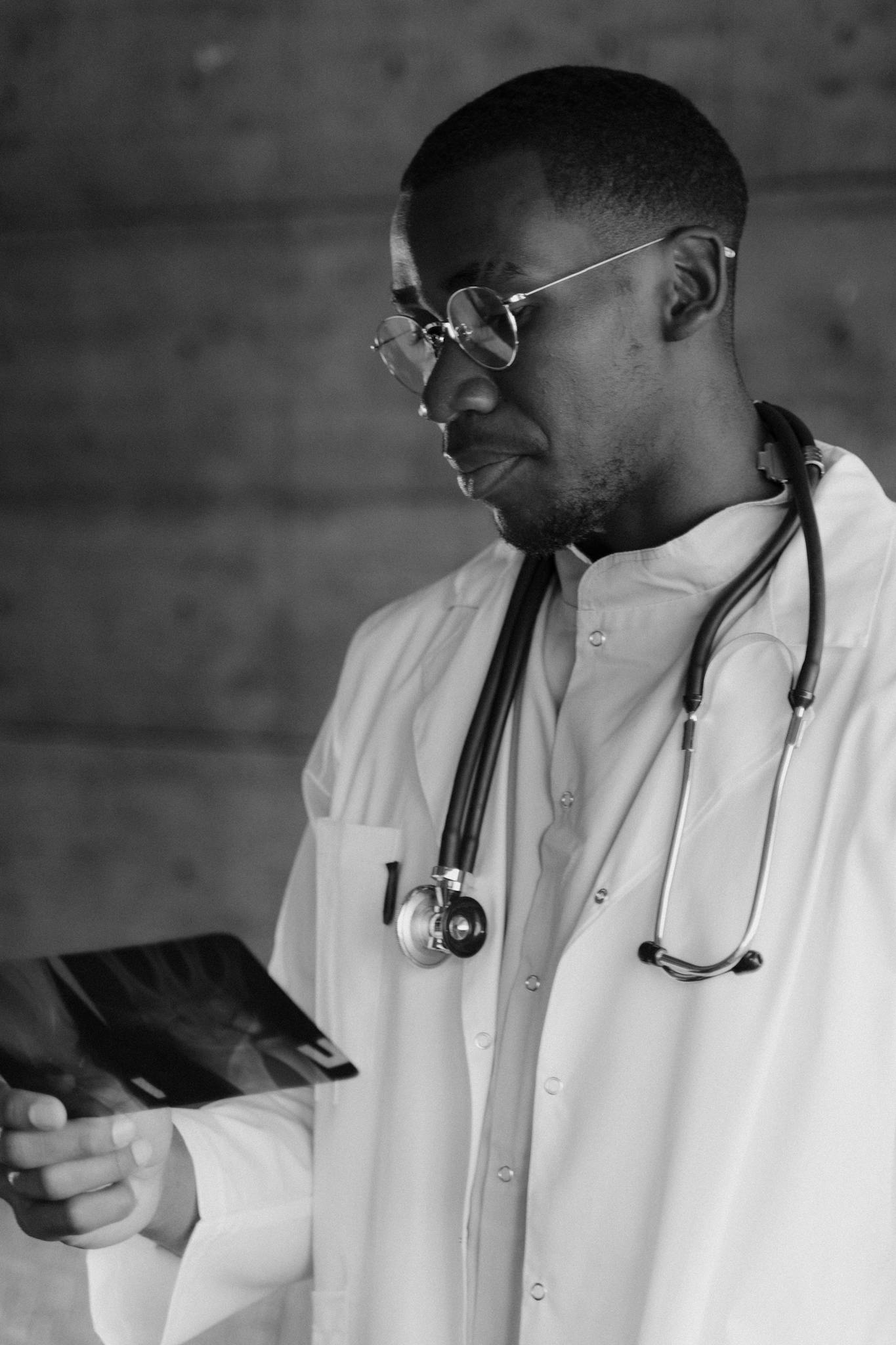 Monochrome image of a doctor examining an X-ray, wearing a stethoscope and lab coat.